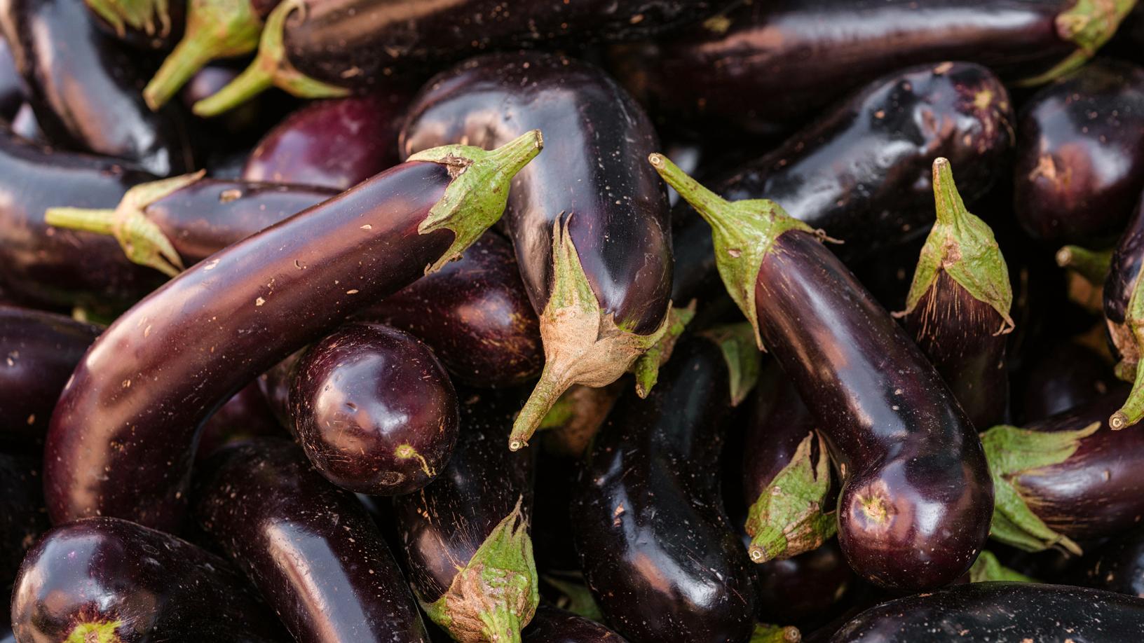 Mehrere Auberginen dicht gestapelt; glatte, dunkelviolette Haut, frische grüne Stiele