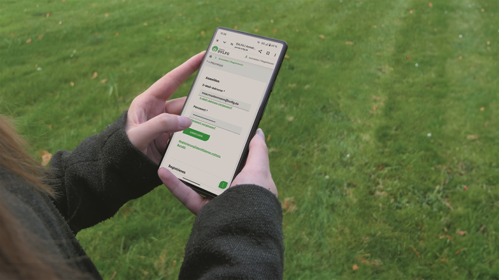 Vergrößerung des Bildes für Bildausschnitt: Eine Person auf einer Wiese, schaut ins Handy und hat die Seite Prämiensystem der SVLFG offen..