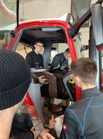 Vergrößerung des Bildes für Zwei junge Männer sitzen in einer Fahrerkabine, zwei stehen davor und halten Informationsmaterial in der Hand. Der jungen Mann auf dem Fahrersitz stellt den Sitz ein. .