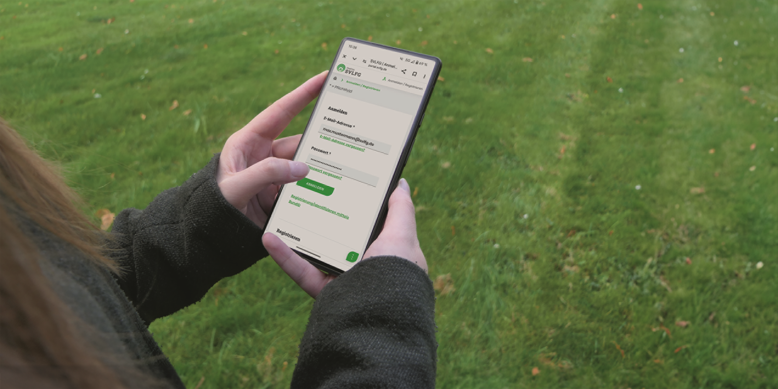 Bildausschnitt: Eine Person auf einer Wiese, schaut ins Handy und hat die Seite Prämiensystem der SVLFG offen.