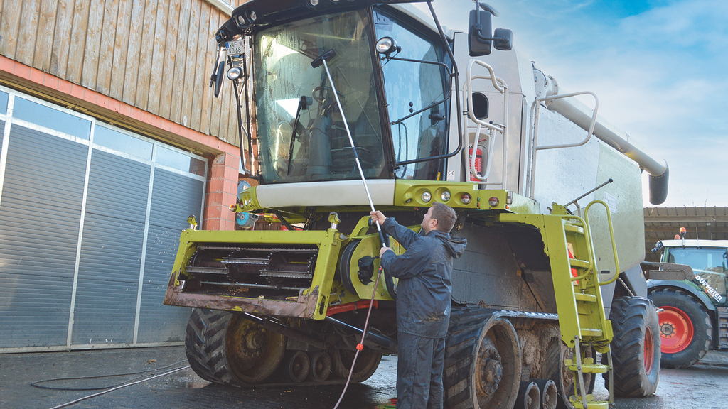 Vergrößerung des Bildes für Ein junger Mann säubert die Scheibe einer landwritschaftlichen Maschine mit Hilfe einer Teleskopstange.