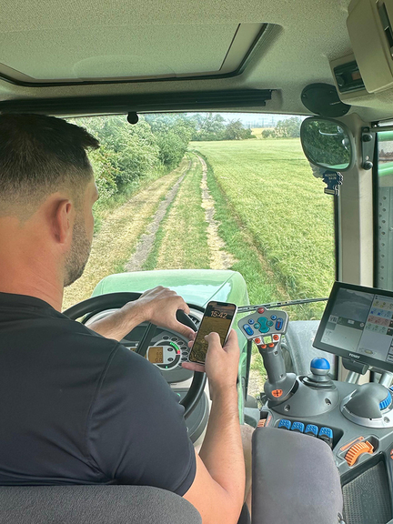 Vergrößerung des Bildes für Mann fährt in einem Traktor und schaut dabei auf sein Handy .