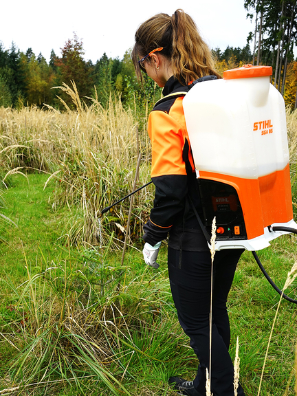 Vergrößerung des Bildes für Eine Person auf einer Wiese in Schutzkleidung mit Rückenspritze bei der Arbeit..