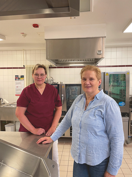 Vergrößerung des Bildes für zwei Frauen stehen in einer Großküche und schauen in die Kamera.