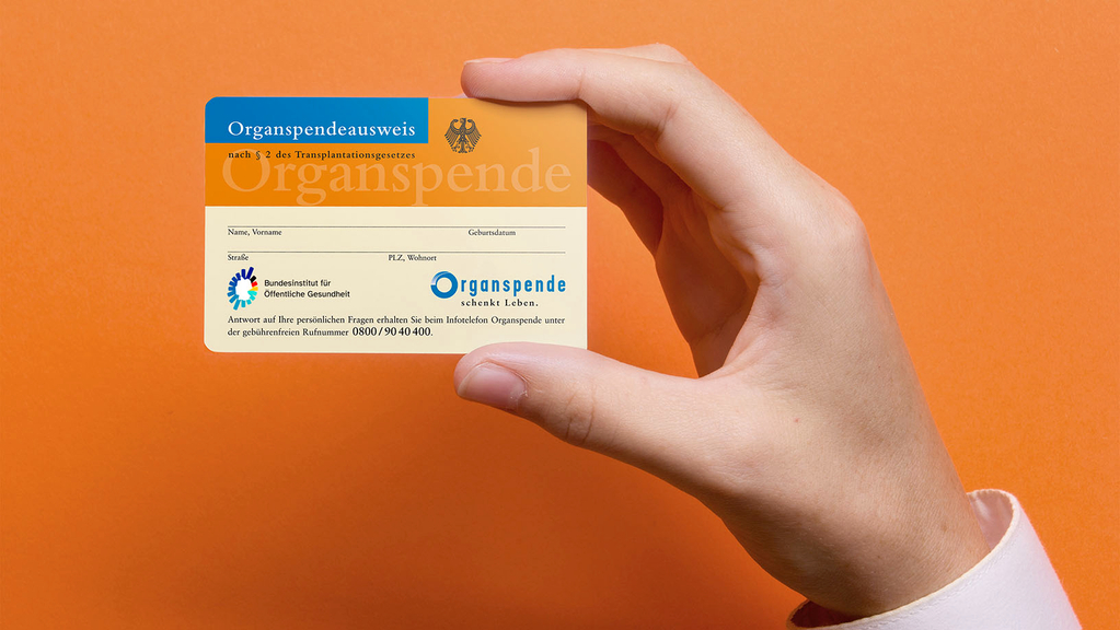 Vergrößerung des Bildes für Hand hält den Organspendeausweis zwischen Zeigefinger und Daumen.