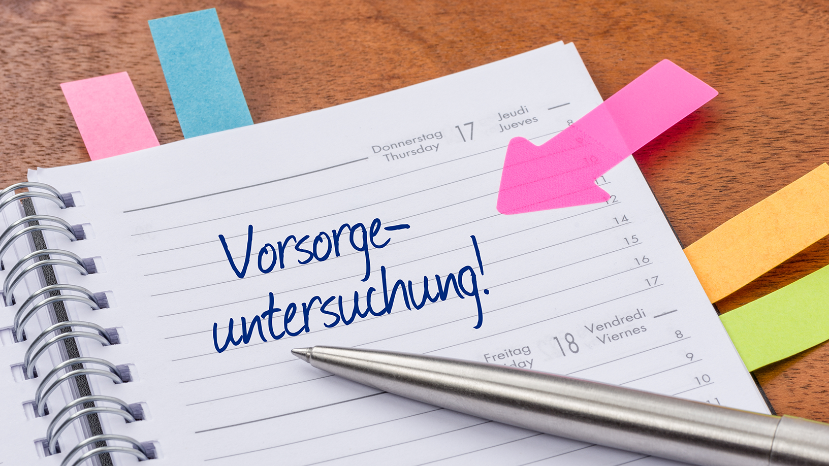 Aufgeschlagene Kalenderbuch-Seite mit dem handschriftlichen Eintrag „Vorsorgeuntersuchung“ in einer Spalte; ein Kugelschreiber liegt quer über dem Papier.
