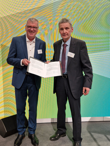 Vergrößerung des Bildes für Zwei Männer stehen nebneinander auf der Bühne und halten den Kooperationsvertrag vor sich.