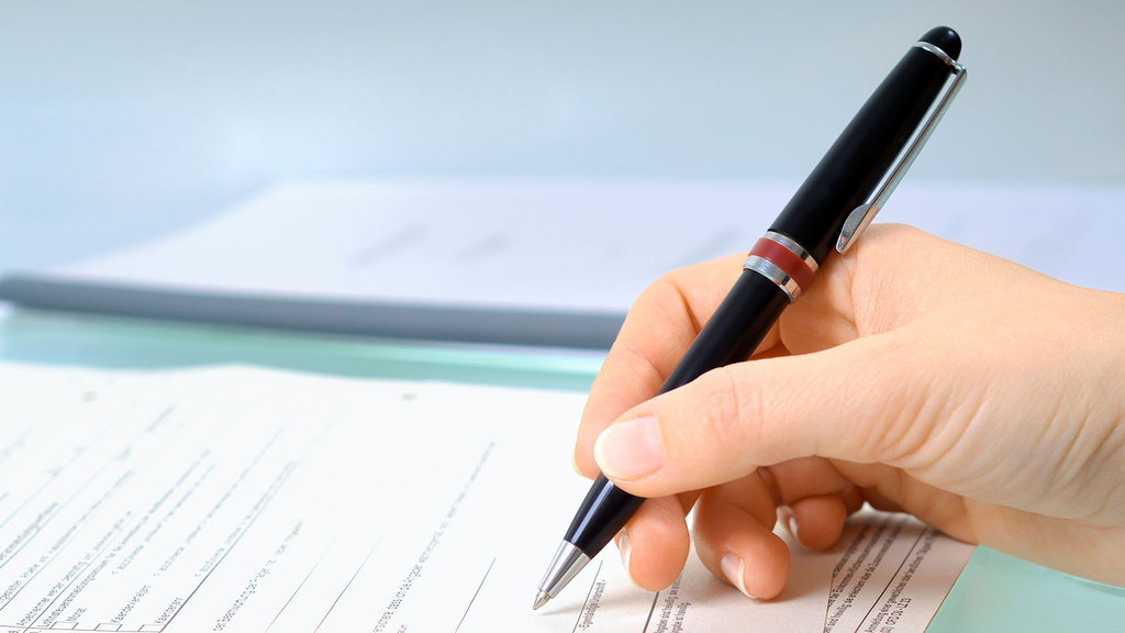 Vergrößerung des Bildes für Ein Blatt Papier liegt auf dem Tisch. Eine Hand hält einen Kugelschreiber und füllt den Fragebogen aus. .