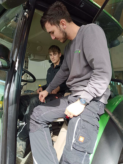 Vergrößerung des Bildes für Zwei junge Männer sitzen in einer Fahrerkabine, einer hält eine Schablone an den Sitz..