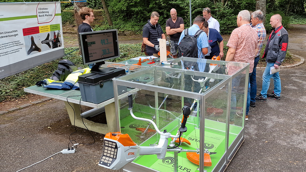 Vergrößerung des Bildes für Menschen stehen an einem Messestand draußen auf dem sich ein Vibrationsstand befindet..