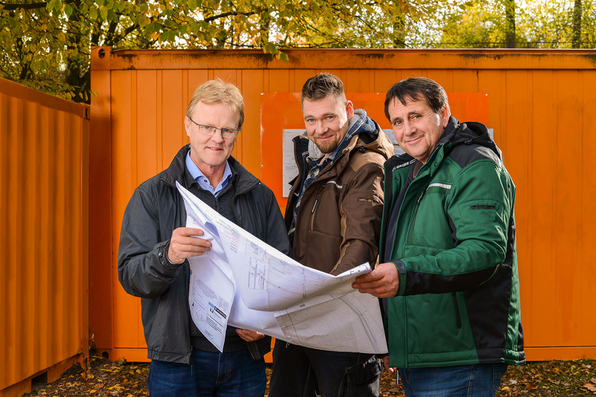 Vergrößerung des Bildes für drei Personen halten einen Plan in der Hand und schauen in die Kamera.