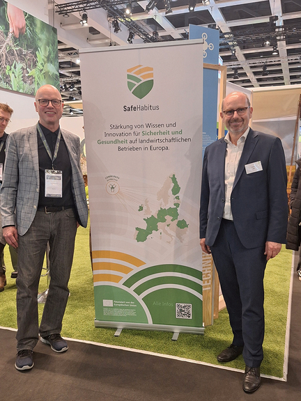 Vergrößerung des Bildes für Zwei Personen stehen auf einer Messe vor einem Plakat mit der Aufschrift Safehabitus..