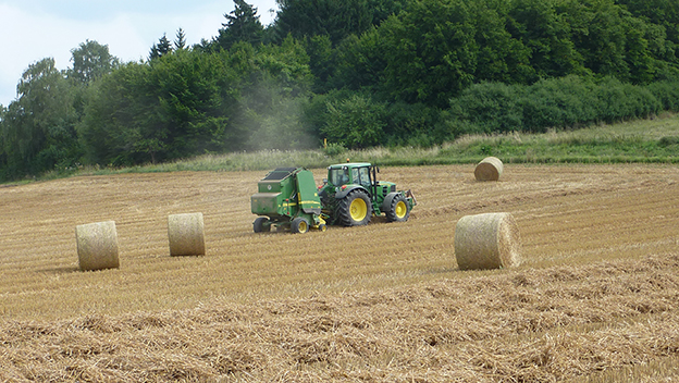 Traktor mit Ballenpresse bei Ernte auf dem Feld