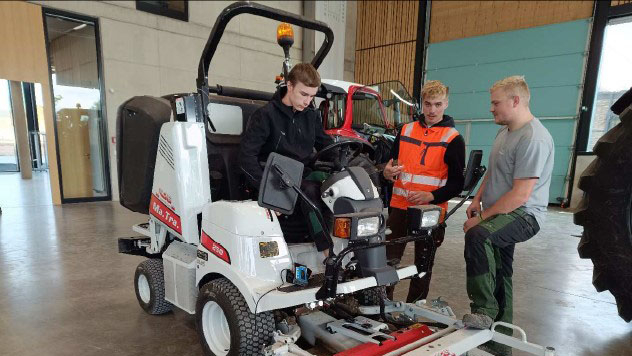 Vergrößerung des Bildes für Drei junge Männer stehen an einer landwirtschaftlichen Maschine und beratschlagen sich..