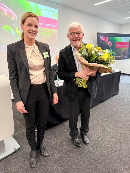 Vergrößerung des Bildes für Frau Schneider steht neben Herrn Empl. Dieser hält einen Blumenstrauß in den Händen. Beide Personen schauen in die Kamera..