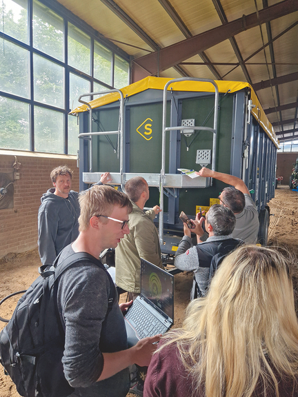 Vergrößerung des Bildes für In einer Halle steht ein landwirtschaftlicher Anhänger. Mehrere Personen stehen davor, schauen ihn sich an, fotografieren, erklären und unterhalten sich. .
