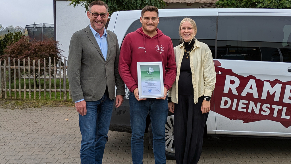 Vergrößerung des Bildes für Es stehen 3 Personen vor einem Auto, die mittlere Person hält das Zertifikat in der Hand..