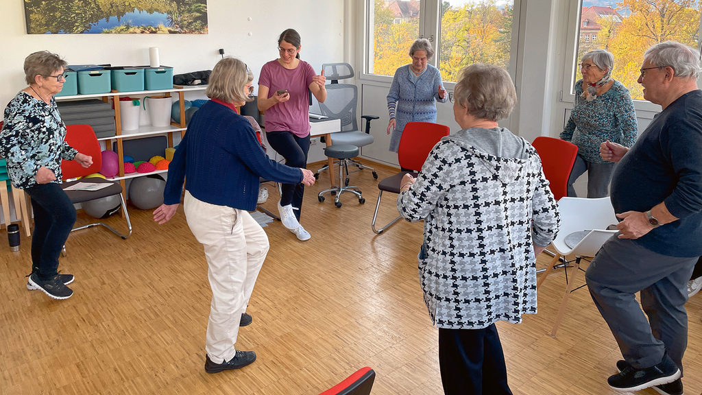 Vergrößerung des Bildes für Mehrere ältere Menschen machen Übungen für das Gleichgewicht uns stehen im Kreis auf einem Bein.
