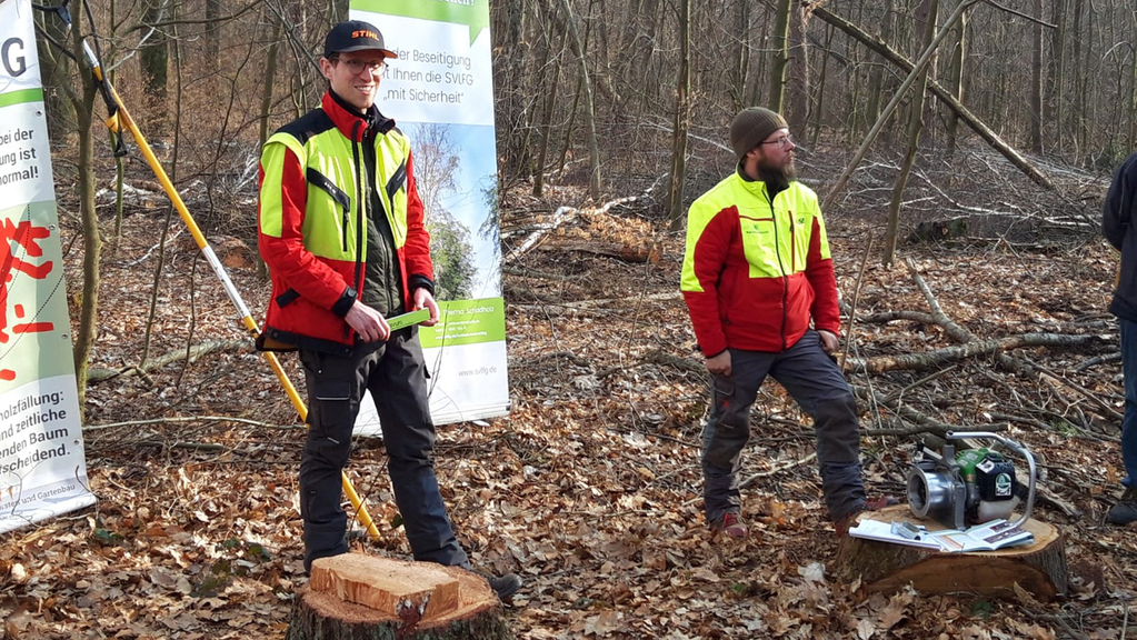Vergrößerung des Bildes für Zwei Männer stehen im Wald und präsentieren eine Spillwinde für die seilunterstützte Fällung..